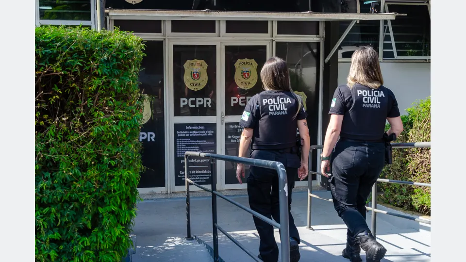 Duas policiais civis caminham em direção à entrada de uma unidade da Polícia Civil do Paraná.