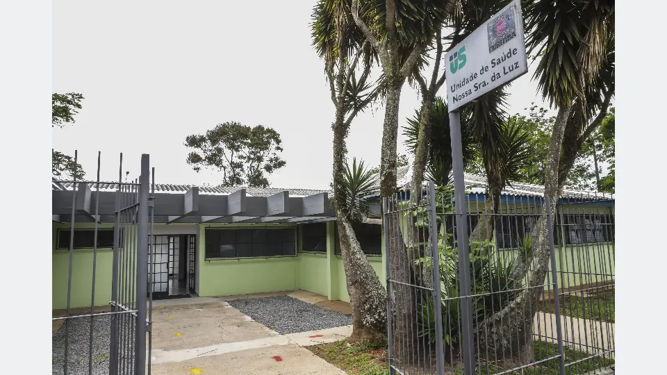 Fachada da Unidade de Saúde Nossa Senhora da Luz, na Cidade Industrial de Curitiba, com portão de entrada e placa de identificação.