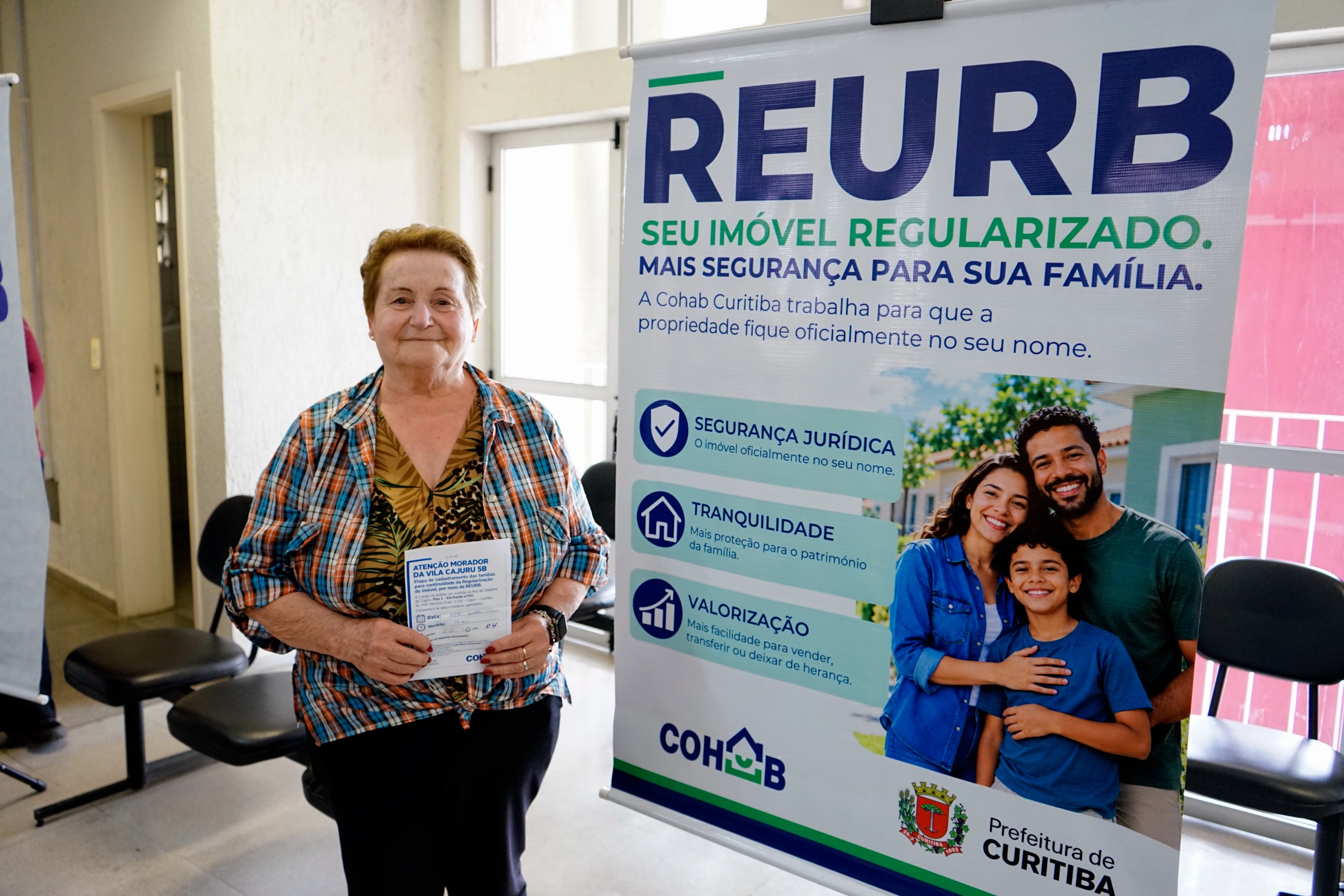 Moradora da Vila Cajuru 5B durante atendimento para regularização fundiária, ao lado de material informativo da Cohab.