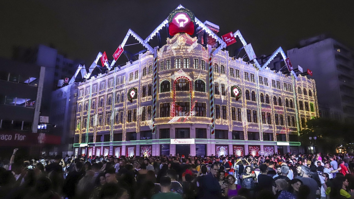 Fachada iluminada do Palácio Avenida durante o Natal de Curitiba, com grande público reunido em frente ao edifício histórico.