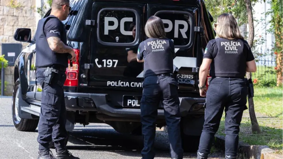 Três agentes da Polícia Civil do Paraná próximos a viaturas policiais em fotografia institucional utilizada para divulgar investigação sobre atestados médicos falsos em Cascavel.