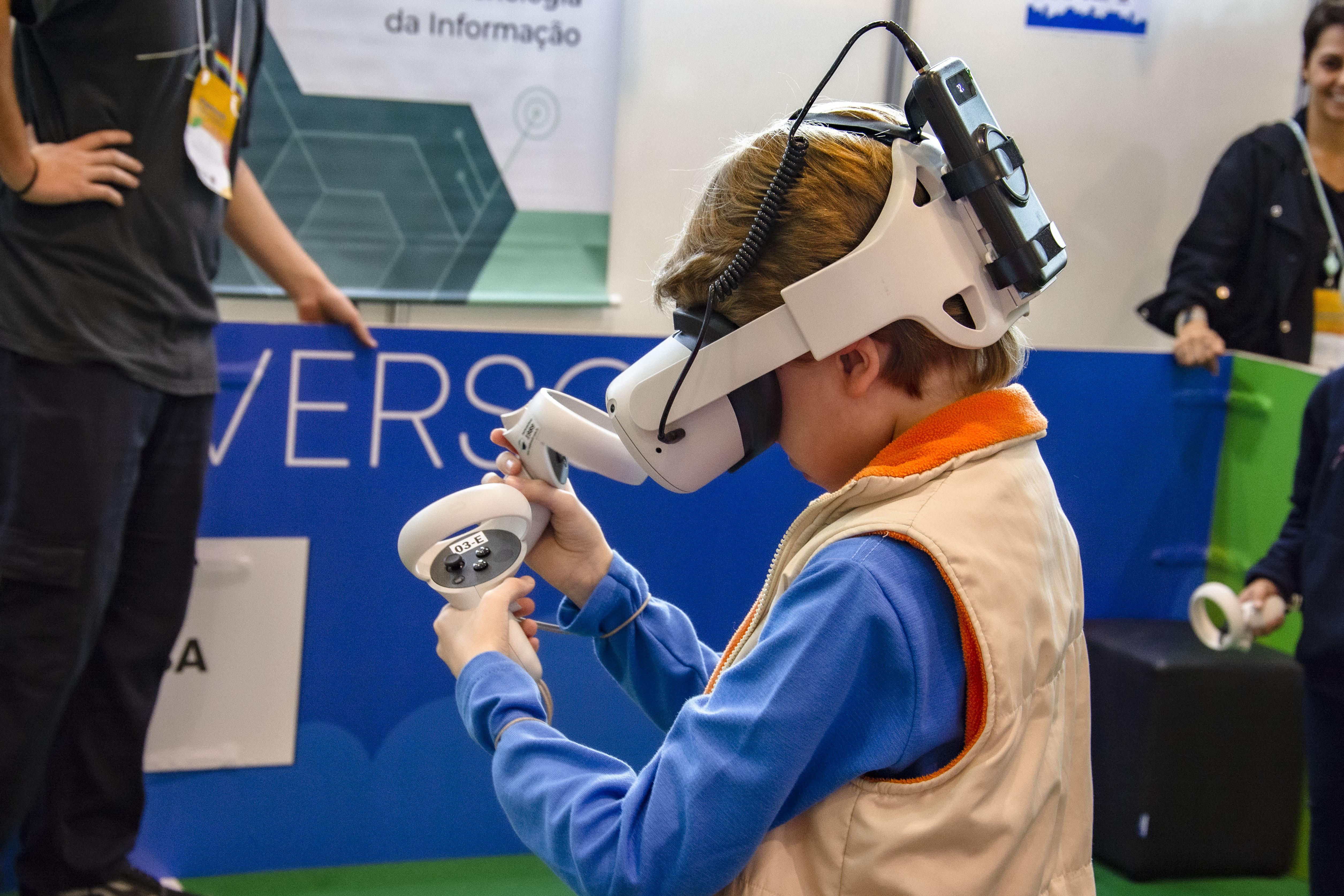 Estudante utiliza óculos de realidade virtual diante de painel de projeto tecnológico durante atividade de inovação em São José dos Pinhais.