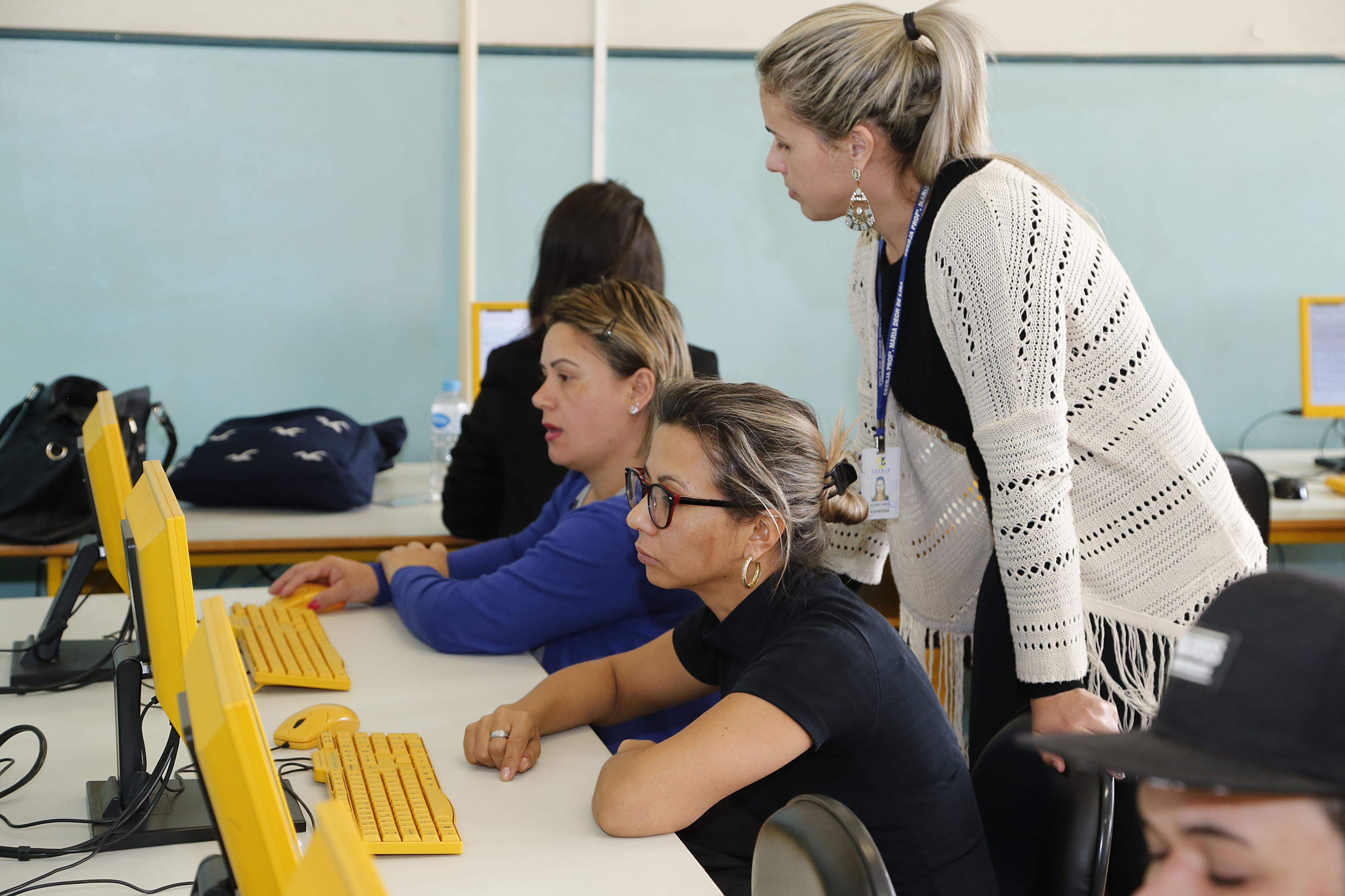 Estudantes adultos utilizam computadores em sala de informática no Paraná.