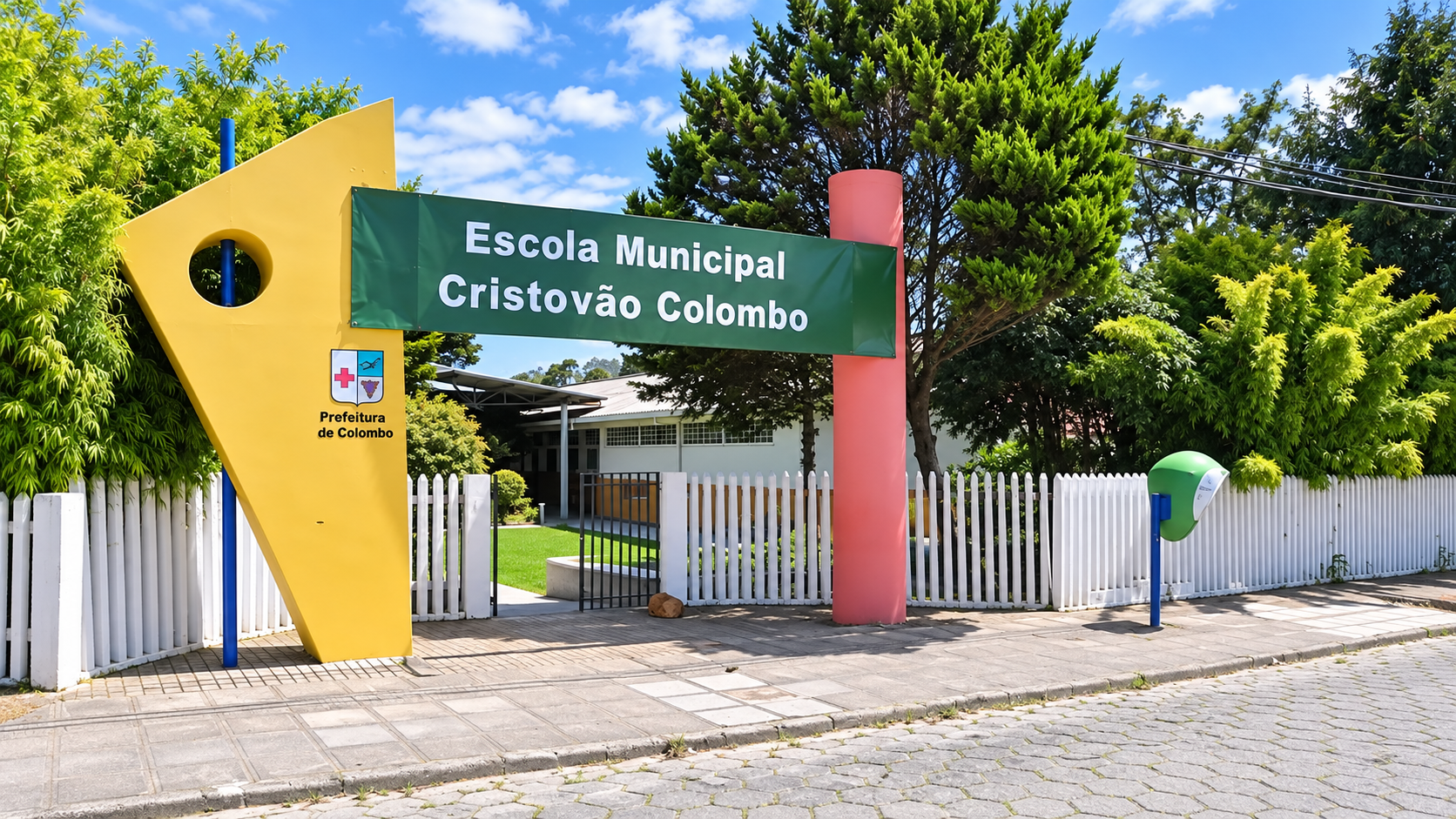 Fachada da Escola Municipal Cristóvão Colombo, em Colombo, no Paraná, com placa de identificação verde, entrada principal, portão e cerca branca.