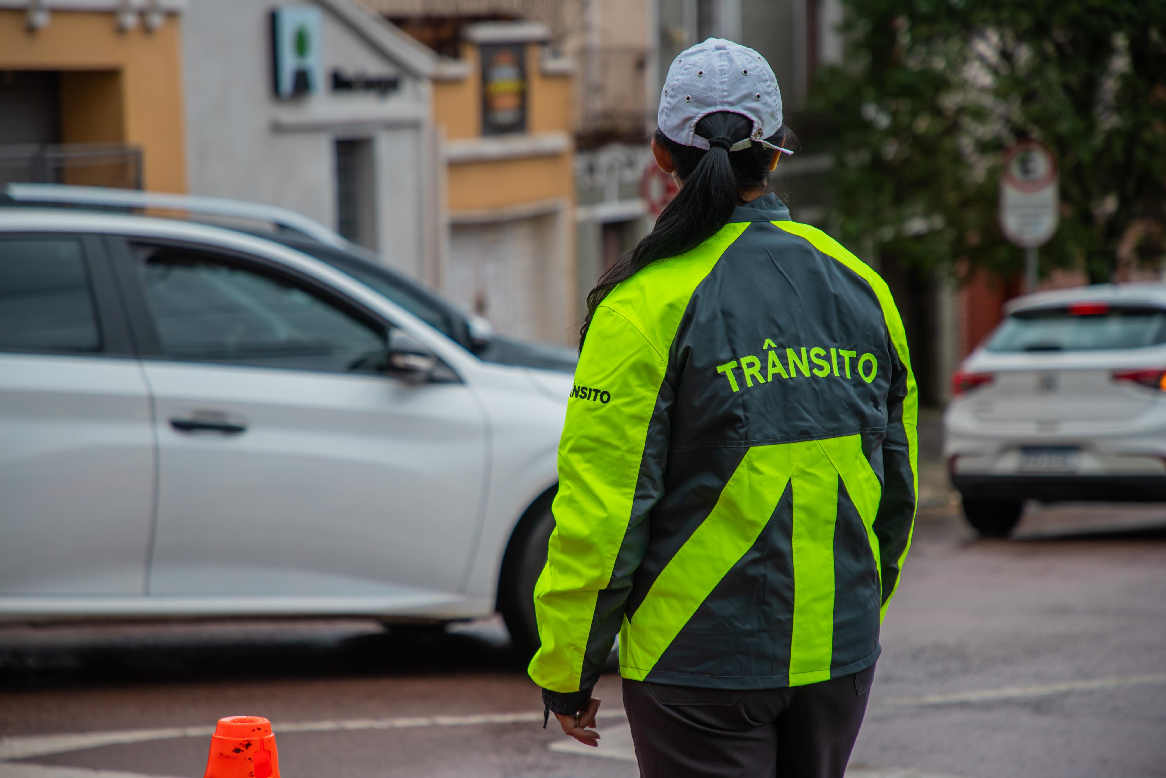 Agente de trânsito de Curitiba ao lado de cones de sinalização e veículos em uma rua da capital paranaense.
