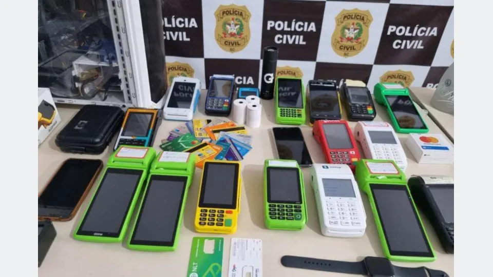 Cartões bancários de diferentes titulares, máquinas de cartão e dinheiro sobre uma mesa, após abordagem policial relacionada a suspeitas de golpes durante show em Curitiba.