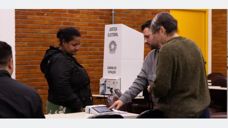 Eleitor vota em urna eletrônica ao lado de uma cabine da Justiça Eleitoral durante as Eleições 2026 no Paraná.