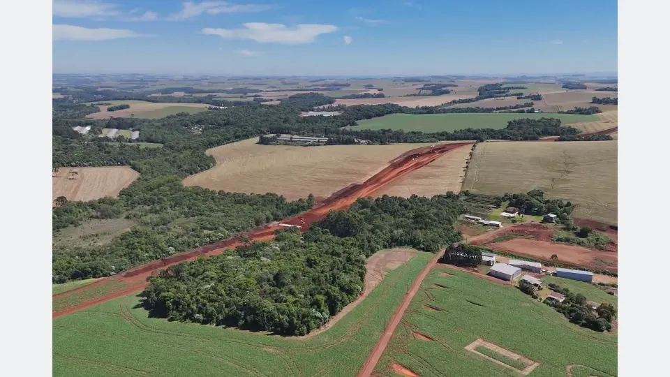 Imagem aérea mostra o traçado em terra vermelha do Contorno Noroeste de Pato Branco, atravessando áreas rurais, lavouras e vegetação durante as obras de construção da rodovia.