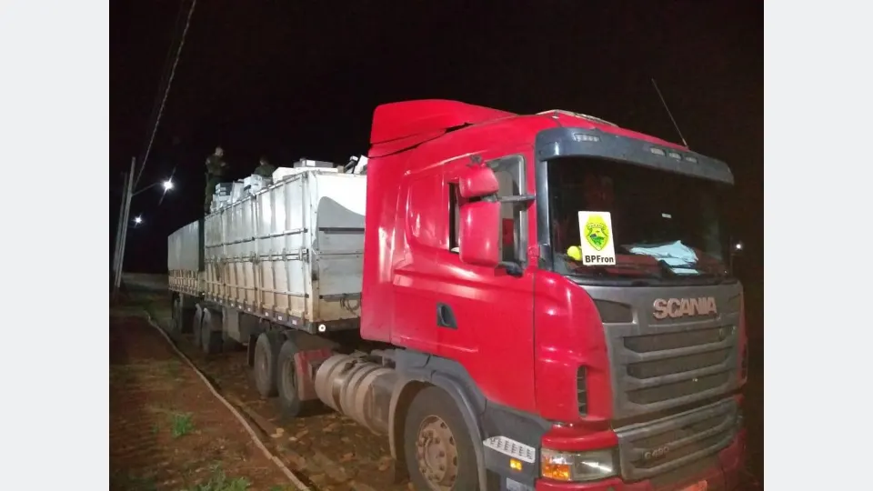 policiais fiscalizando caminhão com caixas de vinho durante operação noturna na fronteira.