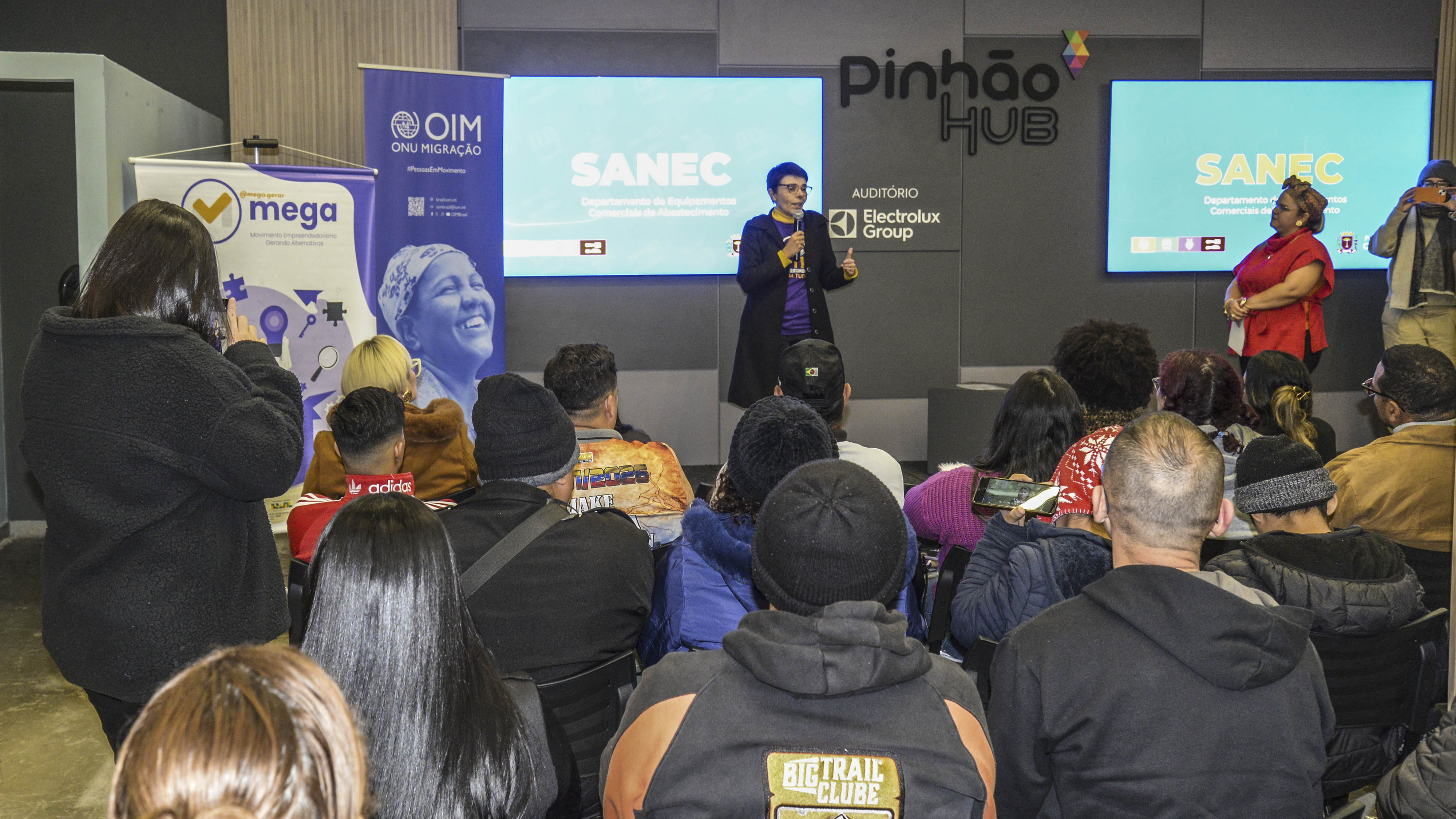 Público acompanha palestra sobre empreendedorismo para migrantes no auditório do Pinhão Hub, em Curitiba.
