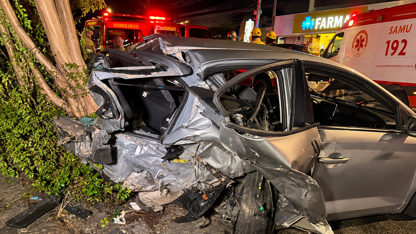 Carro destruído junto a uma árvore durante atendimento de equipes de emergência em Curitiba.