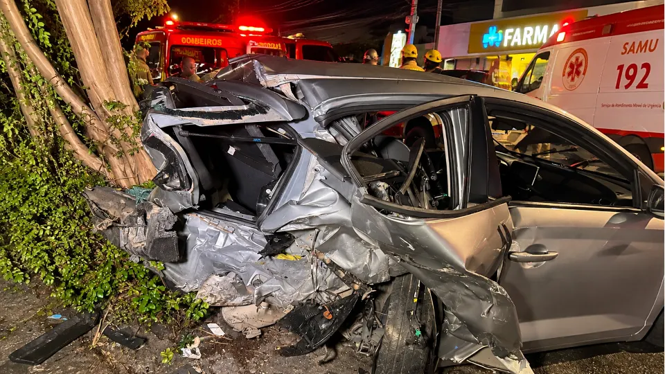 Carro destruído junto a uma árvore durante atendimento de equipes de emergência em Curitiba.