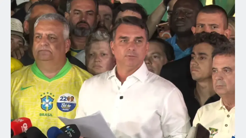 Flávio Bolsonaro, de camisa branca, faz pronunciamento diante de microfones e apoiadores após o segundo turno das eleições presidenciais de 2026.