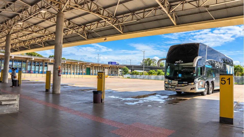Ônibus rodoviário de dois andares da empresa Penha estacionado na plataforma 51 da Rodoferroviária de Curitiba, sob a cobertura do terminal de passageiros.