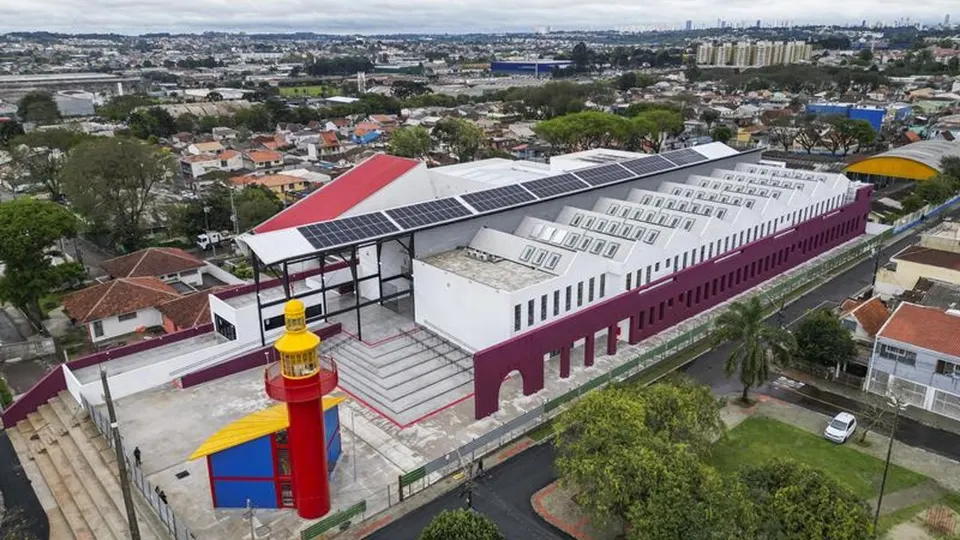 Vista aérea da nova Rua da Cidadania CIC, em Curitiba, mostrando o complexo de atendimento público, os painéis solares, as ruas e as residências da região.