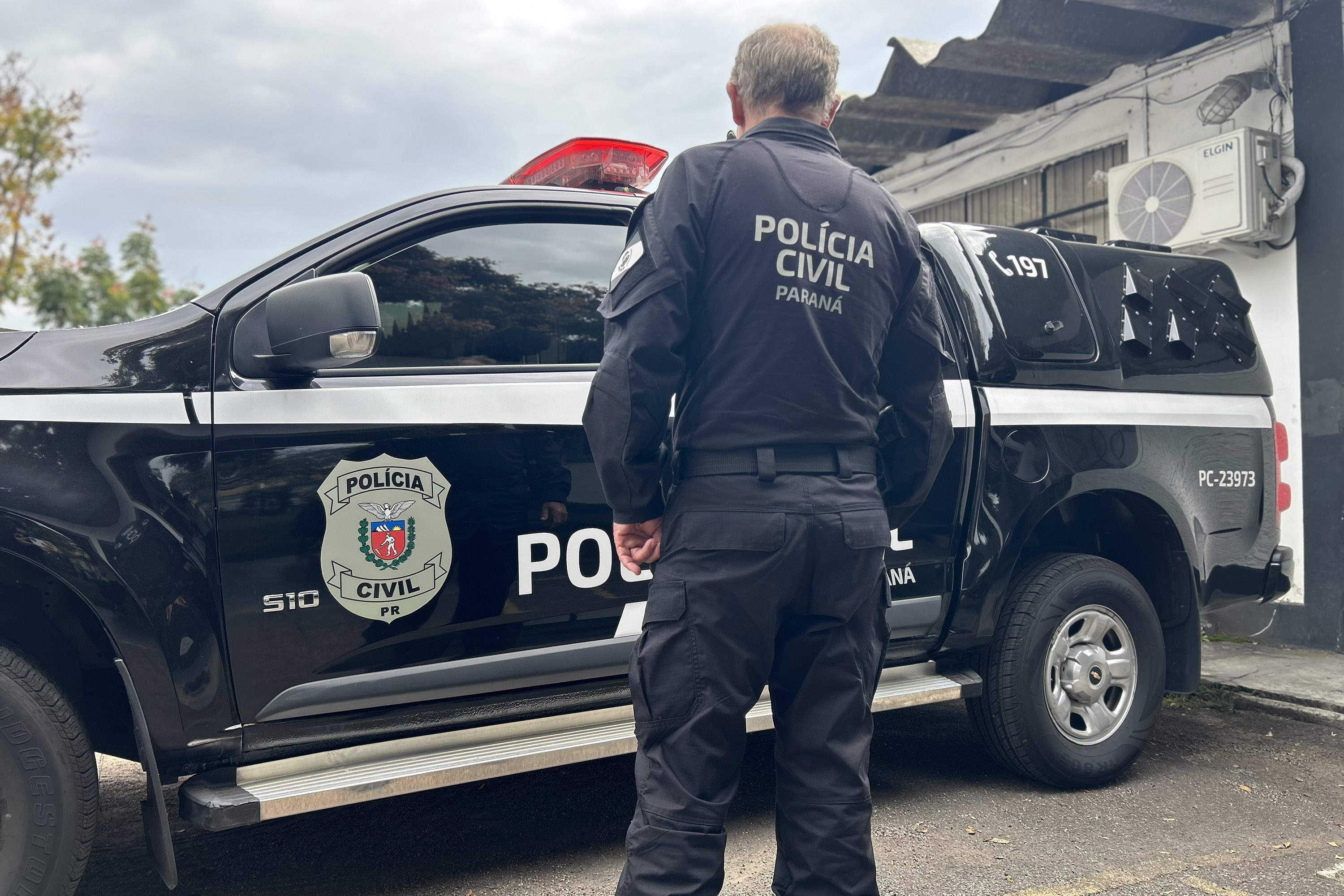 Policial civil de costas ao lado de uma viatura da Polícia Civil do Paraná.
