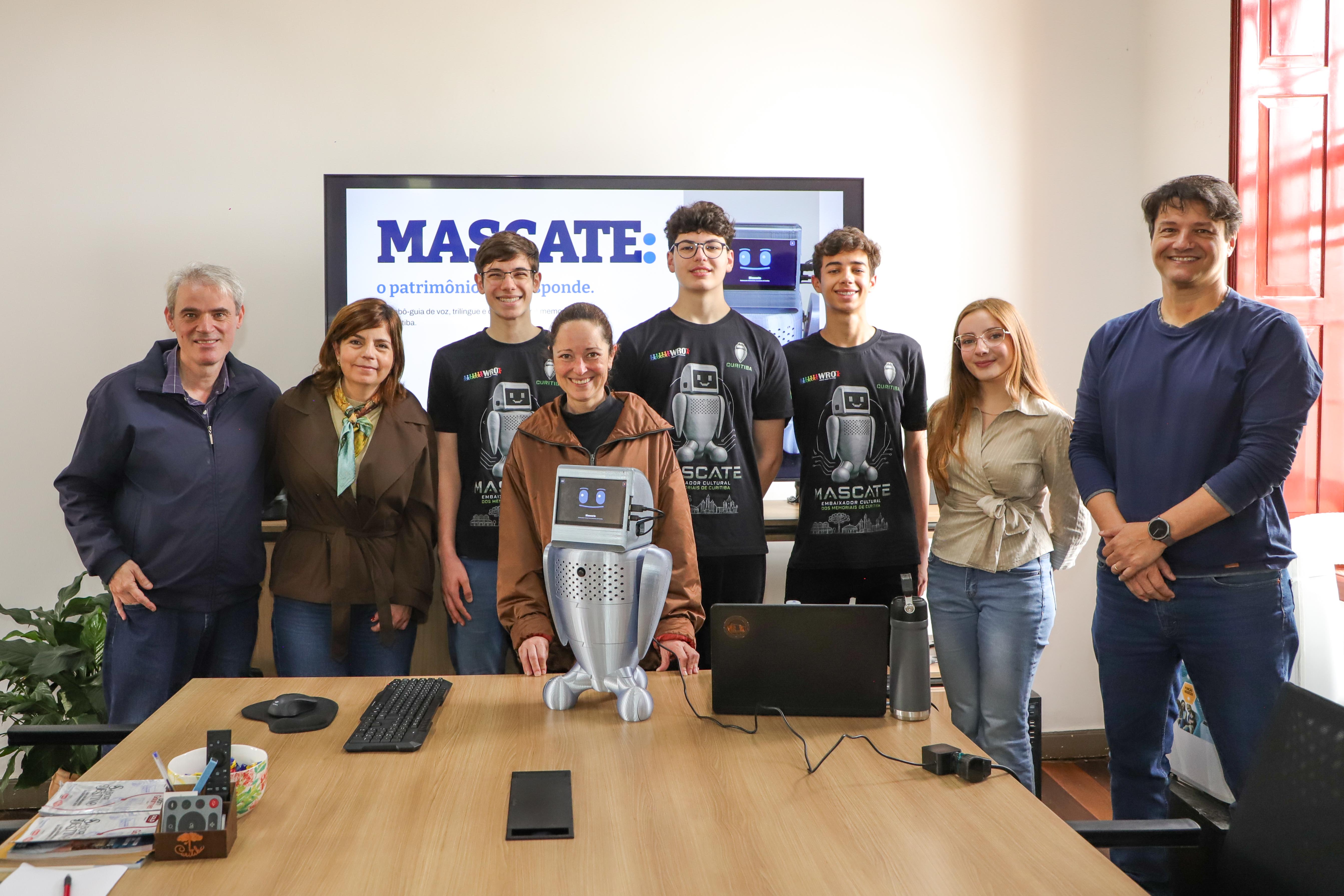 Estudantes e representantes do turismo de Curitiba posam com o robô Mascate, um pequeno equipamento de aparência humanoide.