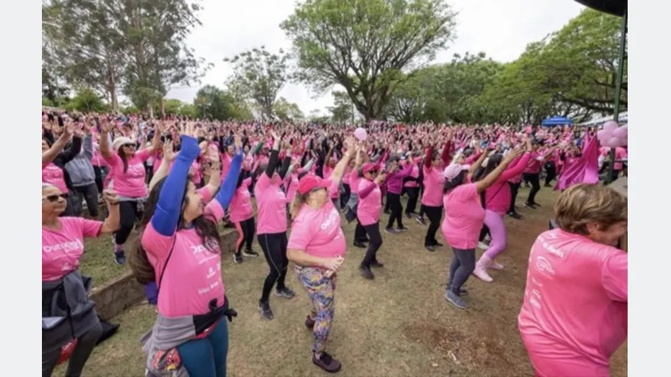 Grupo de pessoas com camisetas cor-de-rosa participa de atividade coletiva de conscientização sobre o câncer de mama.