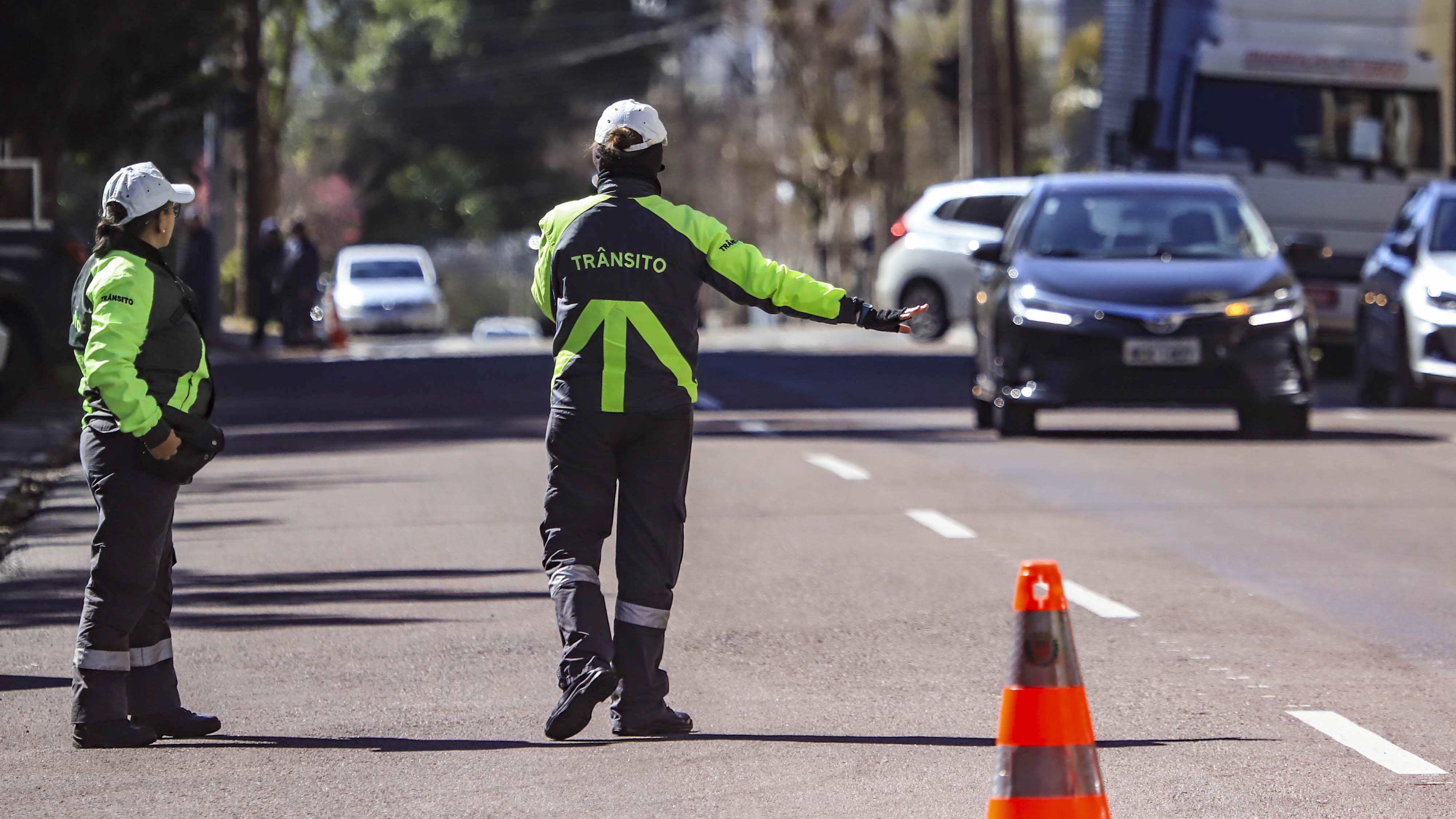 Agente de trânsito de Curitiba ao lado de motocicleta e barreiras de sinalização, em imagem institucional utilizada para ilustrar os bloqueios no entorno da Arena da Baixada.