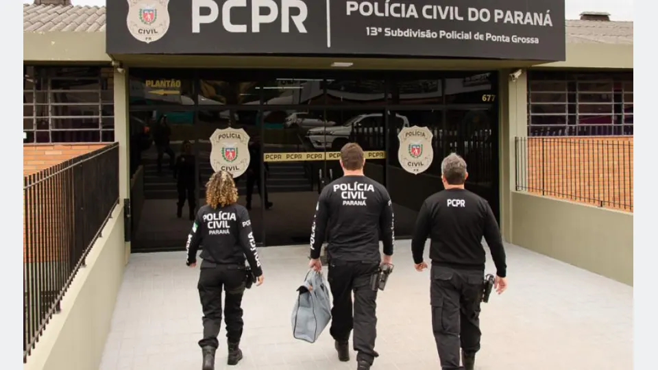 Policiais civis do Paraná de costas, próximos a uma viatura, entrando em uma unidade policial, em fotografia institucional.