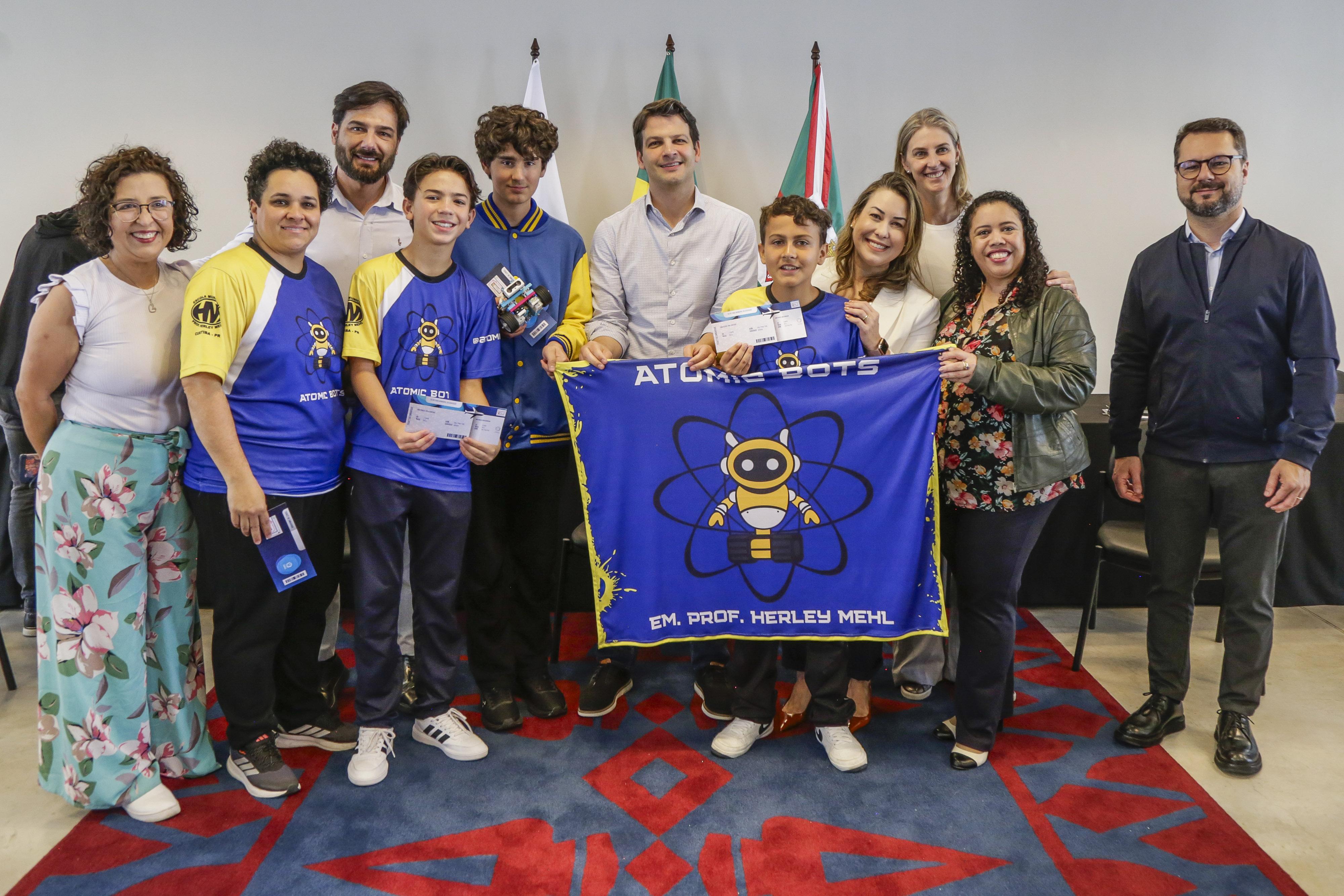 Equipe de robótica Atomic Bots da Escola Municipal Herley Mehl apresenta bandeira azul durante registro de premiação e reconhecimento.